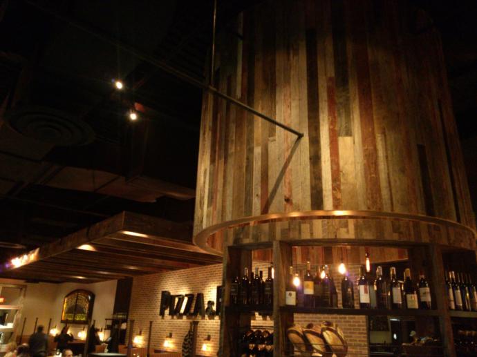 Above the bread station, a cylinder of reclaimed barn siding emphasizes the center of the restaurant, with a curved wine shelf along the front.