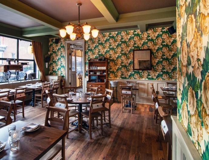 In pursuit of fulfilling the aspiration for a modern take on an old-school tavern, John Derian print wallpaper was incorporated in the restaurant bringing a softer feel and color tones that complement the reclaimed oak flooring.