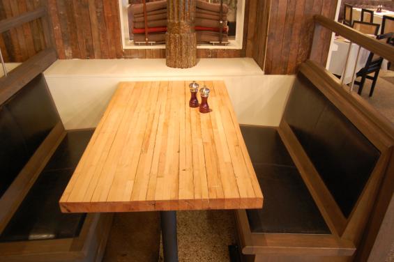 A close-up of the reclaimed bowling lane table shows the original texture and patina of the wood's previous life.